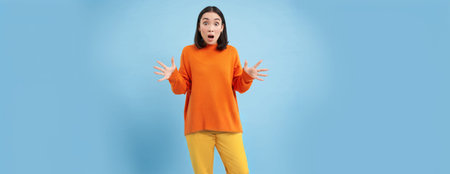 Young asian woman, shakes hands and looks concerned, standing over blue background