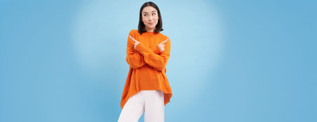 Decisions. Young asian woman points sideways, shows left and right with indecisive smiling face,...