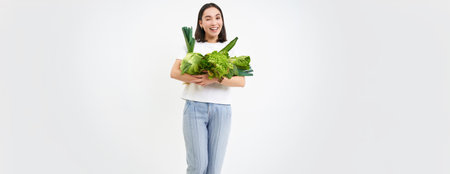 Portrait of happy young woman on green diet, likes eating organic food, holding fresh vegetables from garden, lettuce, cabbage, white studio backgroundの写真素材