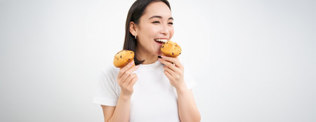 Close up portrait of happy, beautiful smiling woman, eating pastry cupcake, white backgroundの写真素材