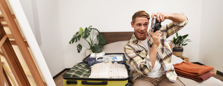 Portrait of handsome man going on vacation, packing suitcase, holding camera, travel photographer going on holidayの写真素材