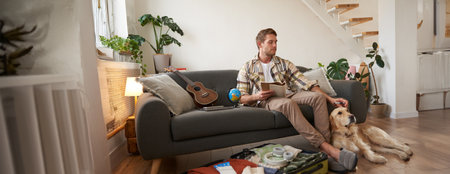 Portrait of man sitting with his dog, packing suitcase for a holiday, going on trip with a petの写真素材