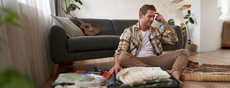 Portrait of guy in panic, packs suitcase, looks stressed and worried, clueless what to bring on holidayの写真素材