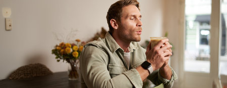 Portrait of young handsome bearded man in coffee shop, sitting on chair, sipping cappuccino, resting in cafeの写真素材