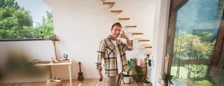 Full length shot of happy traveller, tourist goes on vacation, walks with suitcase, shows smartphone call gesture, leaves the apartmentの写真素材