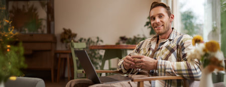Handsome young professional, businessman sitting with glass of coffee and working on laptop,...