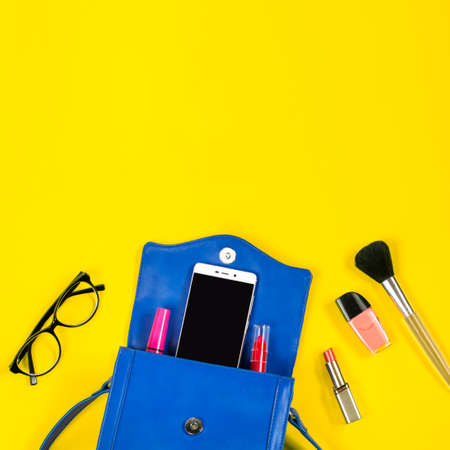 Woman purse, beauty products, smartphone, glasses on a bright yellow background, top viewの写真素材