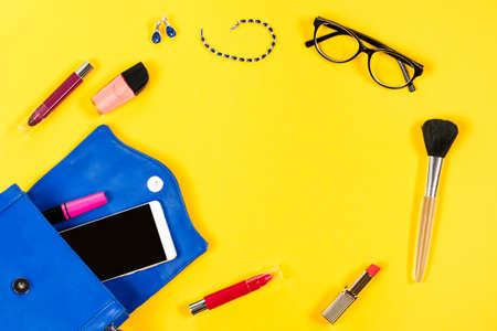 Woman purse, beauty products, smartphone, glasses on a bright yellow background, top viewの写真素材