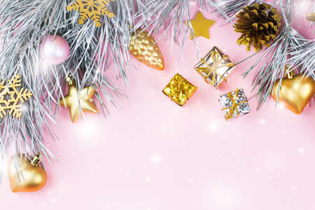Christmas frame with fir branches, conifer cones, christmas ornaments on pastel pink background with snow fallingの写真素材