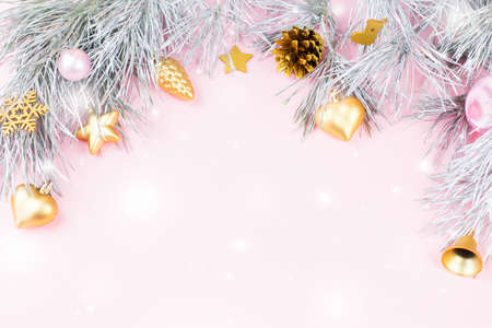 Christmas frame with fir branches, conifer cones and ornaments on pastel pink background with snow fallingの写真素材