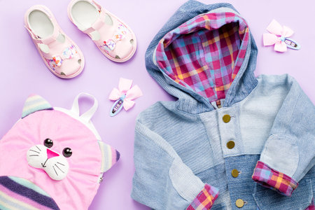 Little girl clothes collection flat lay with denim jacket , sandals, backpack on pastel background.