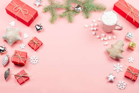 Christmas background with fir tree branches, red giftboxes, decorations, hot drink with marshmallows on pink. Copy spaceの写真素材