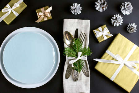 Christmas table setting with plates, silverware, gift box and decorations in black and gold colors. Top viewの写真素材