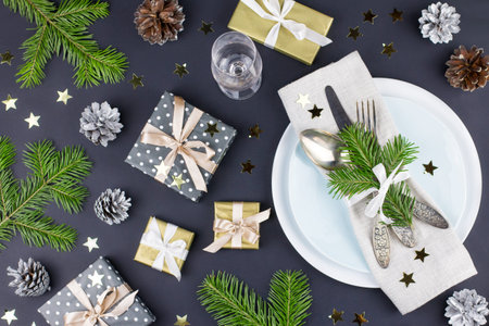 Christmas table setting with plates, silverware, gift box and decorations in black and gold colors....