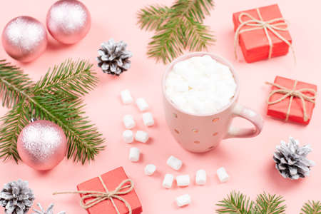 Christmas background with fir tree branches, red giftboxes, decorations, hot drink with marshmallows on pink. Copy spaceの写真素材