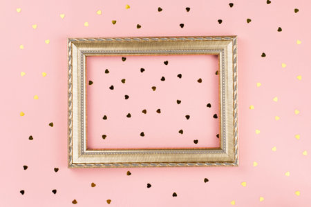 Golden photo frame with space for text, golden confetti on pastel pink background. Valentine's day...
