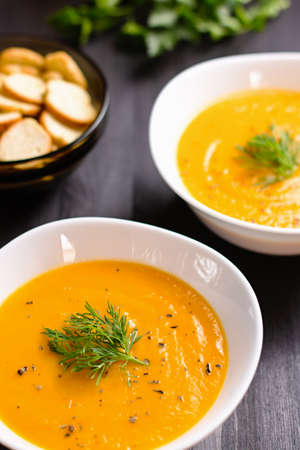 Pumpkin cream soup with croutons and fresh dill and parsley on dark wooden backgroundの写真素材