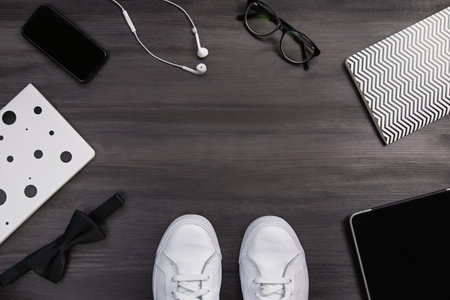 Modern men fashion accessories and electronic devices on dark wooden background. White sneakers,...