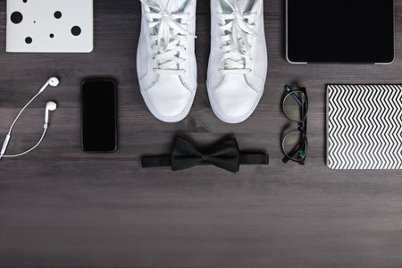 Modern men fashion accessories and electronic devices on dark wooden background. White sneakers,...