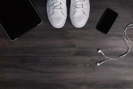 Modern men fashion accessories and electronic devices on dark wooden background. White sneakers, tablet and phone flat layの写真素材