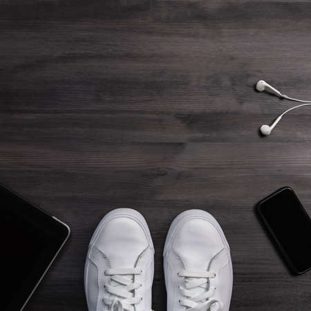 Men accessories with white sneakers, mobile phone, tablet, earphones on dark wooden background, copy spaceの写真素材