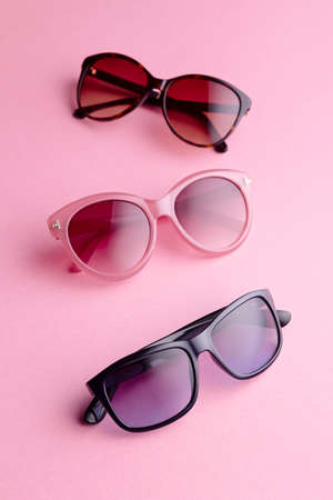 Collection of fashionable sunglasses on pink background. Sunglasses of different shapes and colors flat lay. Oval shaped sunglasses, oversized, wayfarer frames.の写真素材