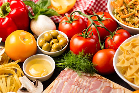 Italian food ingredients with various pasta, vegetables, mushrooms, olives. Flat lay on dark wooden background. Mediterranean cuisine conceptの写真素材