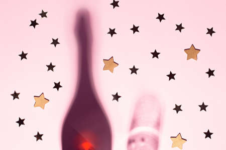 Shadows of champagne bottle and glass with confetti and glitter on pink background. Creative christmas card flat lay. Copy spaceの写真素材