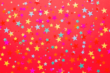 Festive red background with multicolor star shape confetti, copy space. Background for birthdays,...