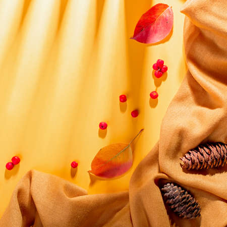 Autumn composition with yellow scarf or blanket, leaves, red berries on sunny yellow background in harsh light. Autumn, fall, halloween, thanksgiving day concept. Flat lay, top view, copy spaceの写真素材
