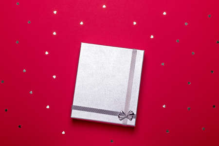 Silver gift box on deep red background with hearts confetti, copy space, top view, flat lay. Background for Valentine's Day, Mother's Day or anniversary. Shopping conceptの写真素材