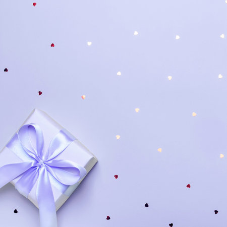 Violet wrapped present or gift box with bow on pastel violet background with hearts confetti, copy space, top view, flat lay. Background for Valentine's Day, Mother's Day or anniversaryの写真素材