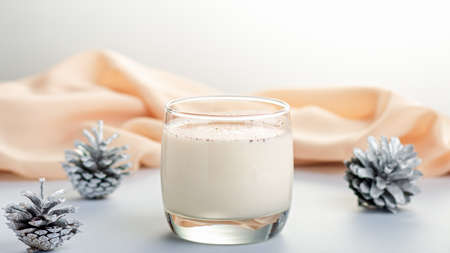 Traditional Christmas cocktail Eggnog with eggs, alcohol, grated nutmeg and cinnamon closeup, copy space. Sweet traditional drink on grey table with beige decorations, burning lanterns and pine conesの写真素材