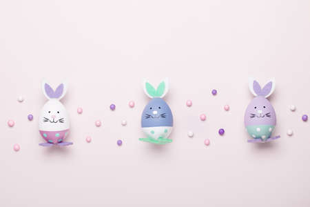 Funny bunny eggs and bunny rabbit ears for kids on pastel pink table top, Easter holiday concept. Easter decoration for kids flat lay, copy spaceの写真素材