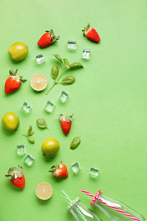 Flat lay with ingredients for summer refreshing drink or smoothie, ice cubes and glass jars on green background, top view. Creative summer drink concept, copy spaceの写真素材
