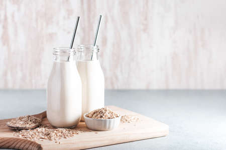 Non dairy oat milk in glass jars with reusable metal straws. Healthy vegan milk alternative still life, copy space. Substitute for traditional cow milk with oat flakes on neutral backgroundの写真素材