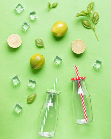 Flat lay with ingredients for summer refreshing drink or smoothie, ice cubes and glass jars on green background, top view. Creative summer drink concept, copy spaceの写真素材