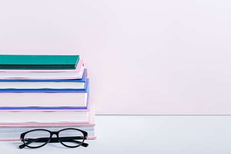 Stack of books on bookshelf with reading glasses against pink wall, still life. Home interior with books, reading conceptの写真素材