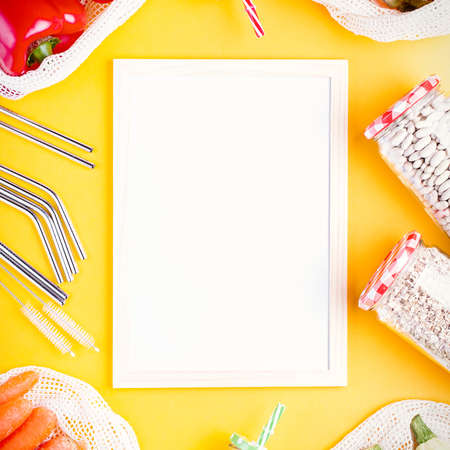 Fresh colorful fruits and vegetables in mesh bags on bright yellow background with white board for text. Zero waste flat lay, copy space. Reusable grocery bags and blank list on yellowの写真素材