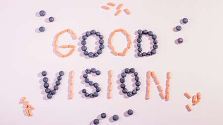 Vitamins and supplements for healthy eyes on pink background. How to maintain good vision concept. Blueberry and orange capsules forming words good visionの写真素材