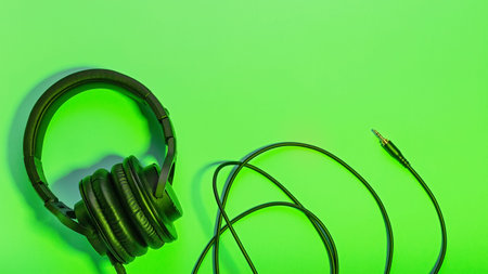 Black massive headphones in female hand on pastel background, copy space. Modern technology flat lay...