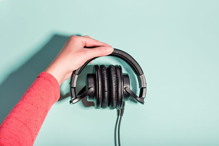 Black massive headphones in female hand on pastel background, copy space. Modern technology flat lay...
