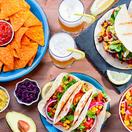 Table with tacos, mango salsa, nachos with sauce, guacamole, lemon beer for Cinco de Mayo celebration party. Appetizers and traditional mexican dishes for family dinner on wooden table top, copy spaceの写真素材
