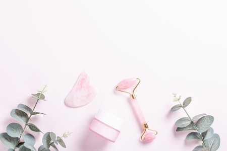 Facial roller, gua sha and moisturizing cream on green leaves. Natural cosmetics and facial tools...