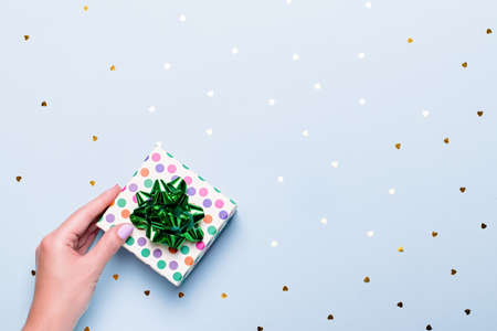 Woman hand holding green gift box on pastel background with confetti, top view, copy space.の写真素材
