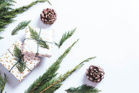 Stylish white and green Christmas flat lay with huge pine cones, cedar branches, presents and...