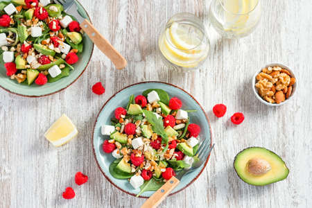 Light salad with raspberry, baby spinach, feta cheese, avocado and walnuts, top view. Fresh original summer salad with lemon water on wooden table topの写真素材