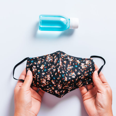 Fashionable protective face mask black with floral pattern and blue hand sanitizer gel on white...