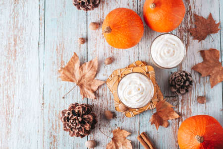 Autumn mood cozy flat lay with pumpkin latte, cedar pine cones, pumpkins and dried leaves on worn wood background, top view, Thanksgiving backgroundの写真素材