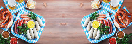 Oktoberfest table with traditional food - roasted sausages, pretzels, beer, sour cabbage on wooden table, top view, bannerの写真素材